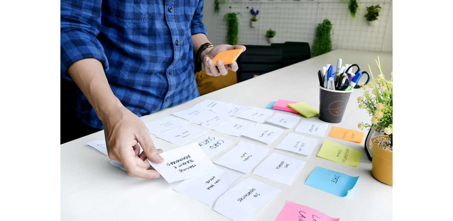 "A man in a blue plaid shirt doing some work organization by setting different sticky notes next to each other